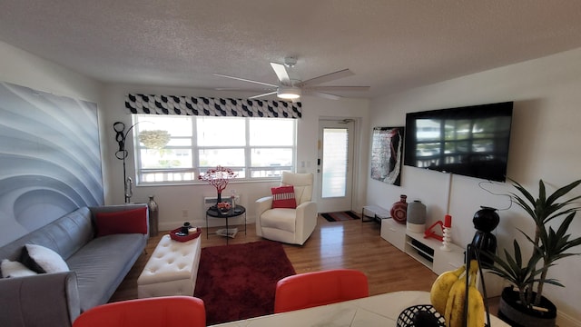 living room featuring ceiling fan, light hardwood / wood-style flooring, and a textured ceiling