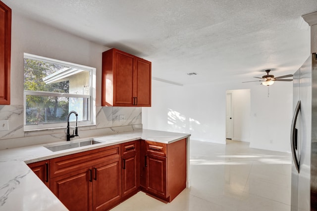 kitchen featuring stainless steel refrigerator, ceiling fan, light stone counters, sink, and tasteful backsplash