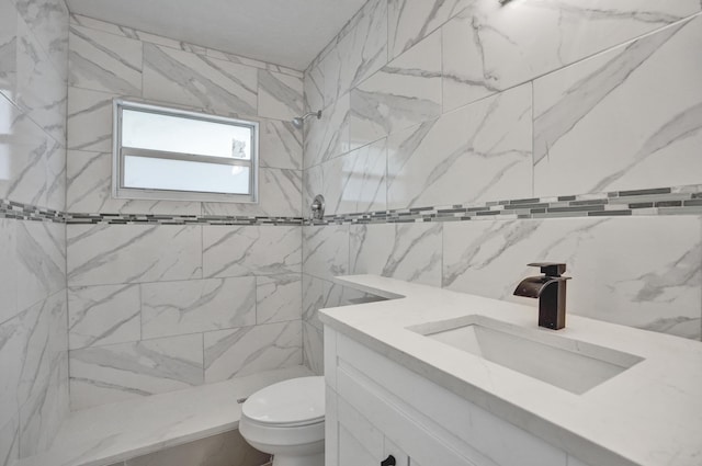 bathroom with toilet, a tile shower, and vanity