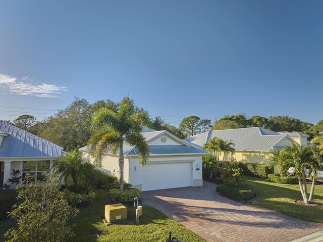 443 11th Sq SW, Vero Beach, FL 32962 - view of front facade featuring decorative driveway, an attached garage, a front lawn, metal roof, and stucco siding