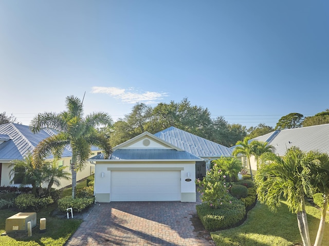 ranch-style house featuring a garage, decorative driveway, metal roof, and stucco siding