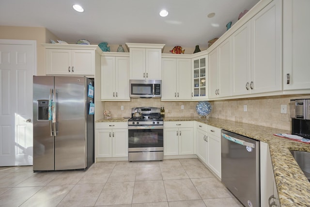 kitchen with light tile patterned floors, decorative backsplash, glass insert cabinets, light stone countertops, and stainless steel appliances