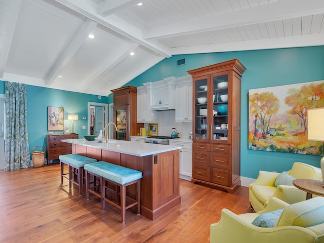 kitchen featuring white cabinets, light wood-type flooring, a kitchen island with sink, and a breakfast bar area