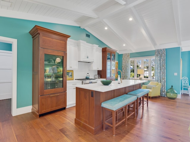 kitchen featuring vaulted ceiling with beams, a center island with sink, white cabinetry, and a breakfast bar area