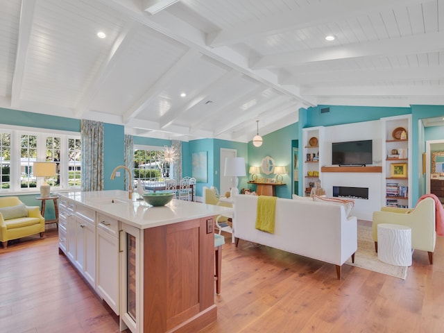 kitchen featuring light wood-type flooring, sink, lofted ceiling with beams, white cabinetry, and an island with sink