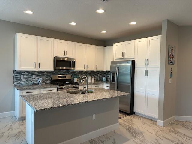 kitchen featuring dark stone countertops, sink, white cabinetry, an island with sink, and stainless steel appliances