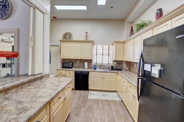 kitchen featuring light stone countertops, a sink, black appliances, tasteful backsplash, and light wood-type flooring