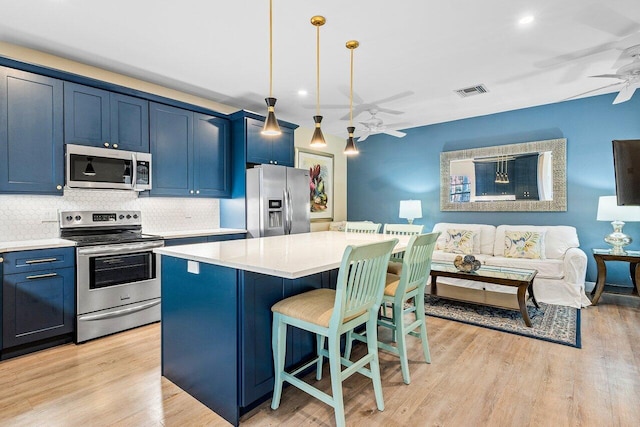 kitchen featuring hanging light fixtures, appliances with stainless steel finishes, blue cabinets, and a kitchen island