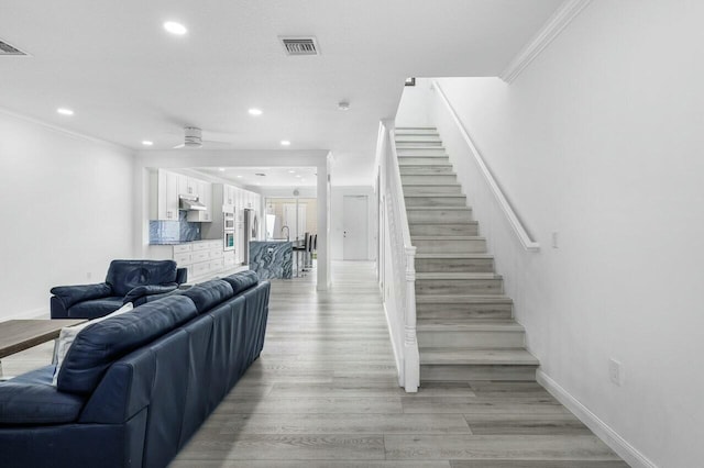 stairs with wood-type flooring, ceiling fan, and crown molding