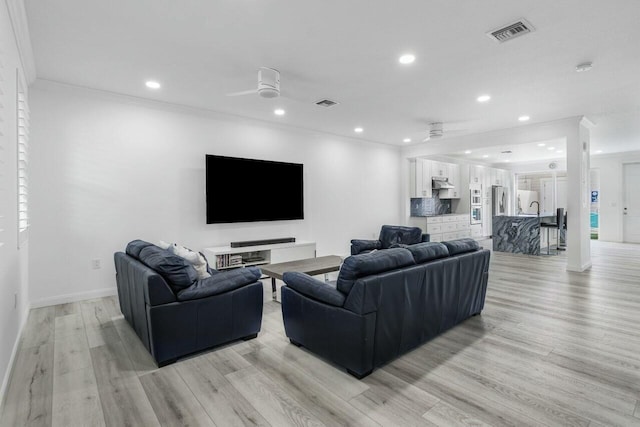 living room featuring sink, light wood-type flooring, ceiling fan, and crown molding