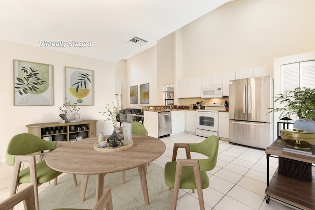 kitchen with light tile patterned floors, visible vents, a high ceiling, appliances with stainless steel finishes, and white cabinets