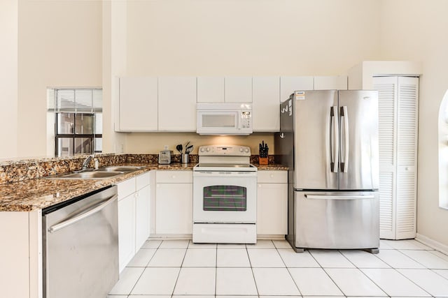 kitchen featuring white cabinets, dark stone counters, stainless steel appliances, and a sink