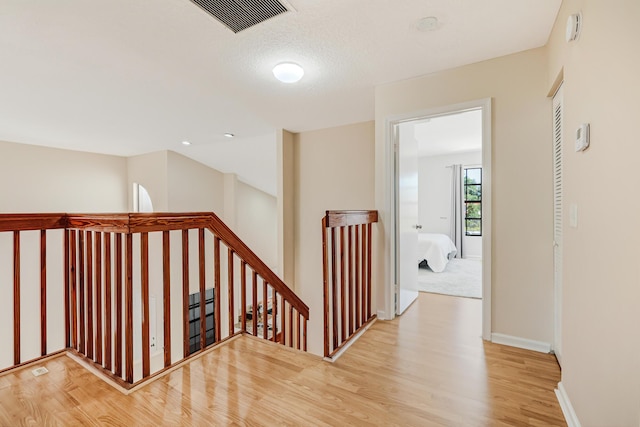 corridor featuring light wood-type flooring, baseboards, visible vents, and an upstairs landing