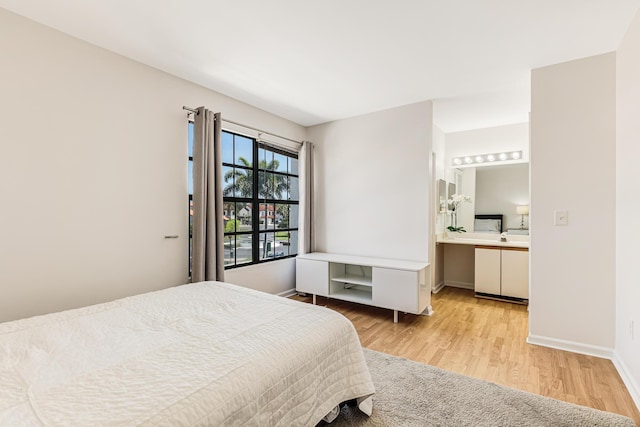 bedroom featuring baseboards, ensuite bath, and light wood finished floors