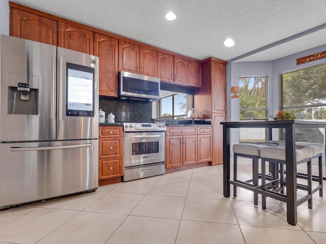 kitchen featuring a textured ceiling, backsplash, light tile patterned floors, and stainless steel appliances