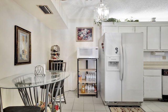 kitchen featuring white appliances, a textured ceiling, light tile patterned floors, an inviting chandelier, and white cabinetry