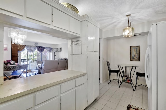 kitchen featuring white refrigerator, light tile patterned floors, a textured ceiling, decorative light fixtures, and white cabinetry