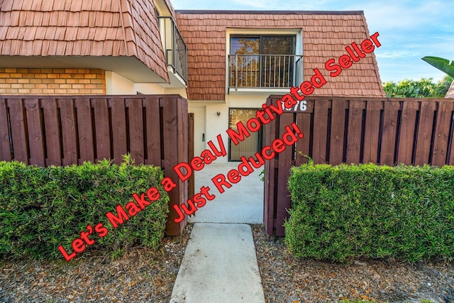 entrance to property with brick siding, stucco siding, mansard roof, and fence