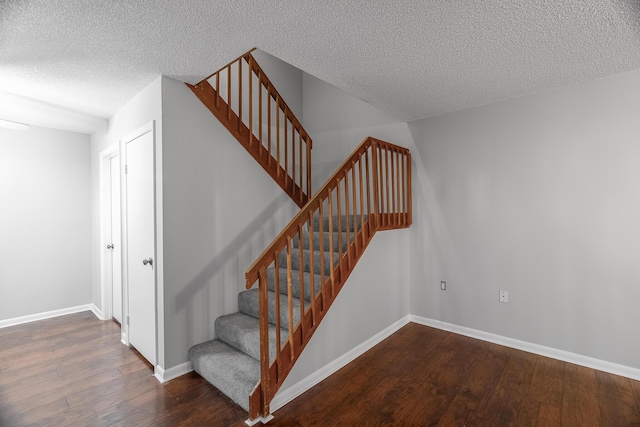 stairway with a textured ceiling, baseboards, and wood finished floors