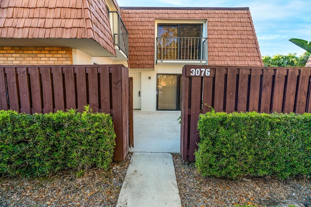 doorway to property with brick siding, stucco siding, mansard roof, and fence