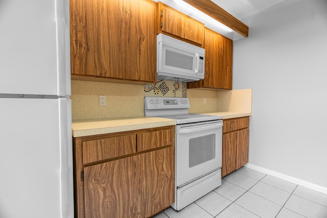 kitchen with backsplash, light countertops, light tile patterned floors, brown cabinetry, and white appliances