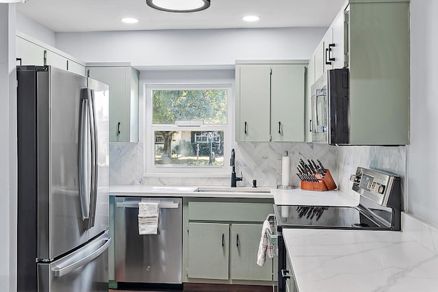 kitchen with sink, tasteful backsplash, green cabinets, stainless steel appliances, and light stone countertops