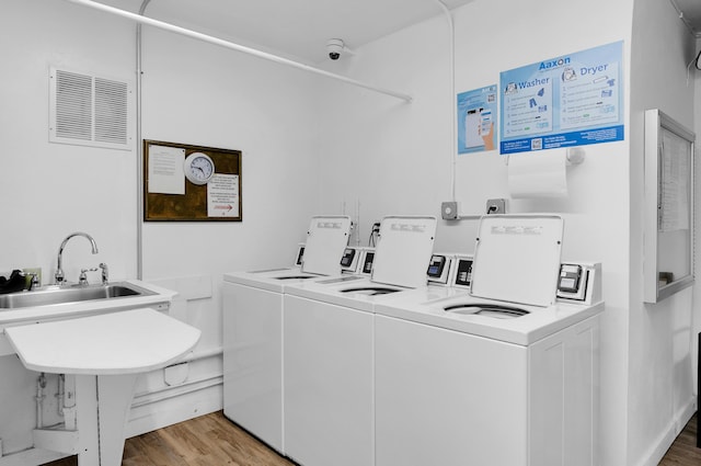 clothes washing area featuring wood-type flooring, separate washer and dryer, and sink