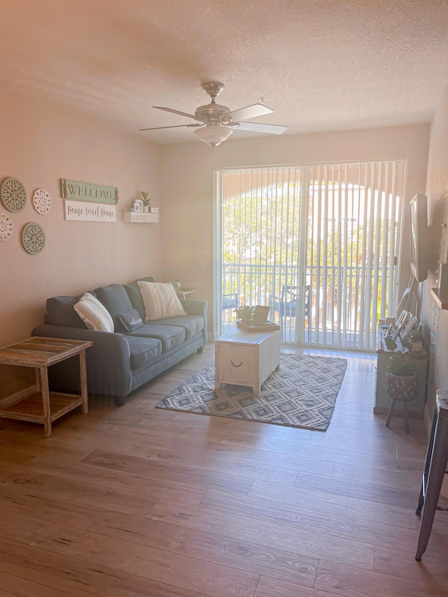 living room featuring wood-type flooring, a textured ceiling, and ceiling fan