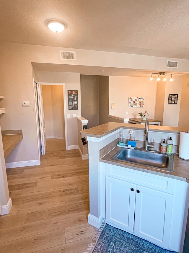 kitchen with kitchen peninsula, white cabinetry, sink, and light hardwood / wood-style flooring