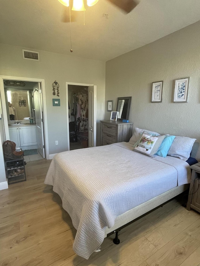 bedroom with ensuite bathroom, sink, ceiling fan, light wood-type flooring, and a closet