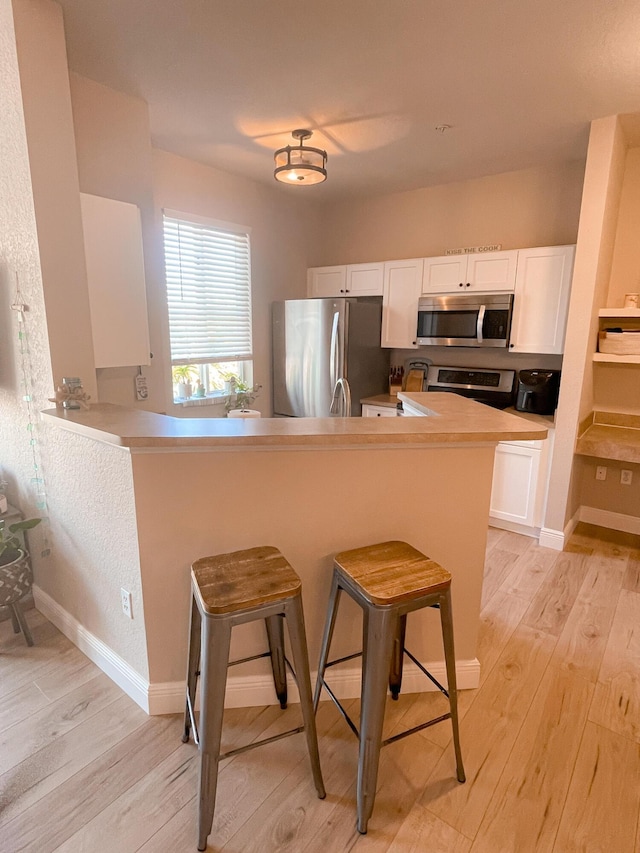 kitchen with a breakfast bar, kitchen peninsula, stainless steel appliances, and white cabinets