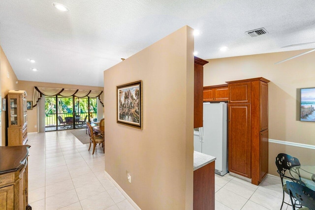 hallway featuring light tile patterned flooring, a textured ceiling, and vaulted ceiling