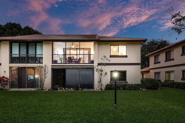 back house at dusk with ceiling fan and a lawn