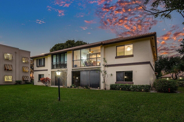 back house at dusk with a yard, ceiling fan, and a balcony