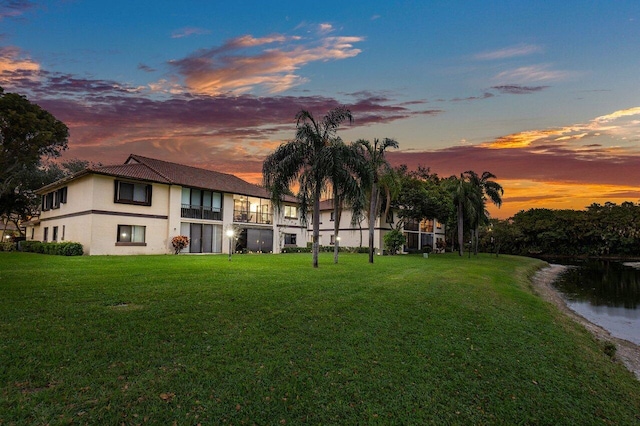 back house at dusk featuring a yard and a water view