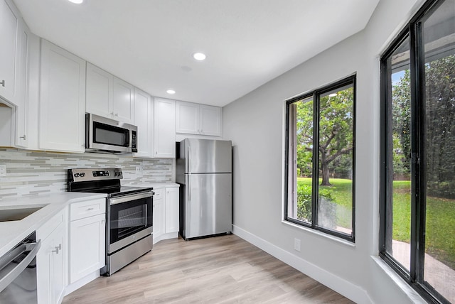 kitchen featuring appliances with stainless steel finishes, backsplash, light hardwood / wood-style flooring, and white cabinetry