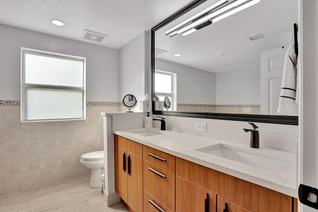 bathroom with vanity, toilet, and tile walls