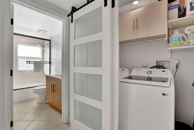 washroom featuring cabinets, a barn door, washing machine and dryer, a textured ceiling, and light tile patterned floors