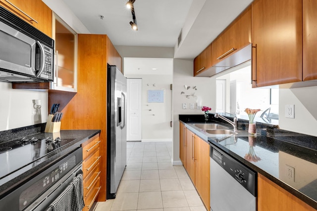 kitchen featuring dark stone counters, rail lighting, sink, light tile patterned flooring, and stainless steel appliances