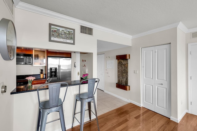 kitchen featuring ornamental molding, a textured ceiling, light hardwood / wood-style floors, a kitchen bar, and stainless steel appliances