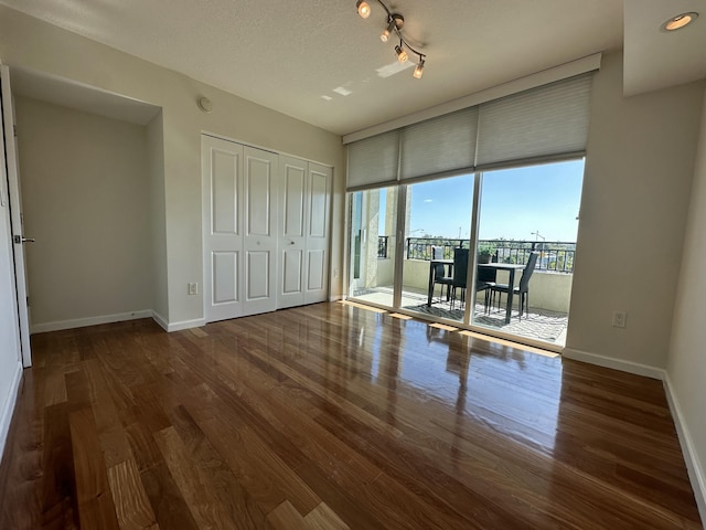 unfurnished bedroom featuring dark hardwood / wood-style floors, access to exterior, a textured ceiling, a wall of windows, and a closet