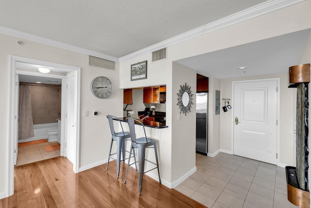 kitchen featuring light tile patterned floors, a textured ceiling, ornamental molding, a kitchen bar, and stainless steel refrigerator