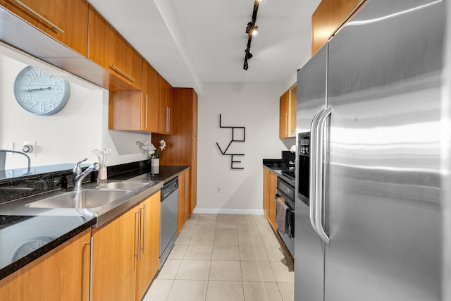 kitchen with sink, dark stone countertops, track lighting, light tile patterned floors, and appliances with stainless steel finishes