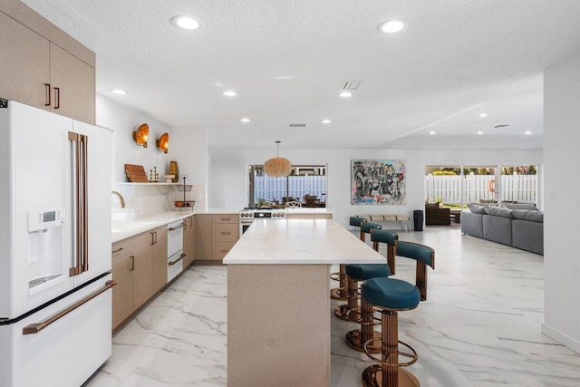 kitchen featuring sink, a textured ceiling, a kitchen bar, light brown cabinetry, and high end appliances