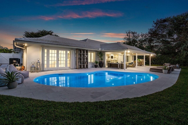 pool at dusk featuring a patio area, french doors, and an outdoor hangout area