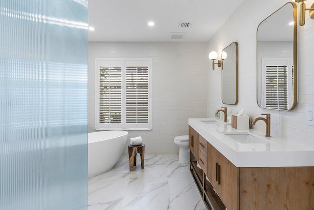 bathroom featuring vanity, toilet, a tub to relax in, and a wealth of natural light