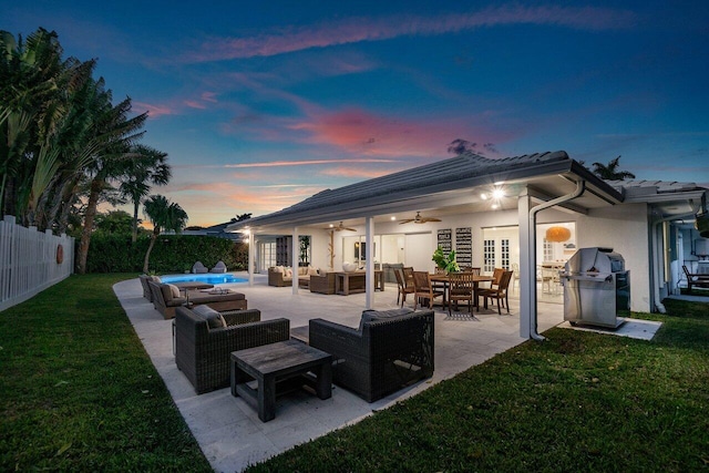 patio terrace at dusk with ceiling fan, area for grilling, an outdoor living space, and a yard