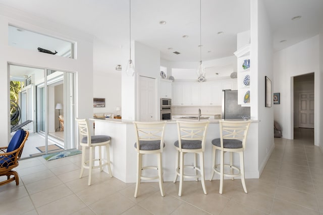 kitchen with kitchen peninsula, stainless steel appliances, pendant lighting, light tile patterned floors, and white cabinetry