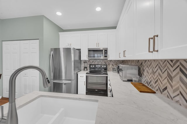 kitchen featuring sink, appliances with stainless steel finishes, tasteful backsplash, light stone counters, and white cabinetry