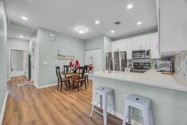 kitchen featuring backsplash, a kitchen breakfast bar, kitchen peninsula, white cabinetry, and stainless steel appliances